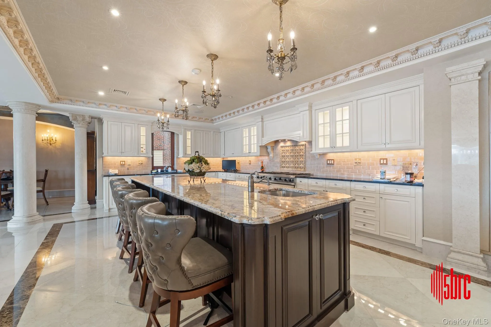 Kitchen featuring inlaid floor details, ornate columns, dark brown cabinetry, light marble finish flooring, and backsplash Kitchen featuring inlaid floor details, ornate columns, dark brown cabinetry, light marble finish flooring, and backsplash