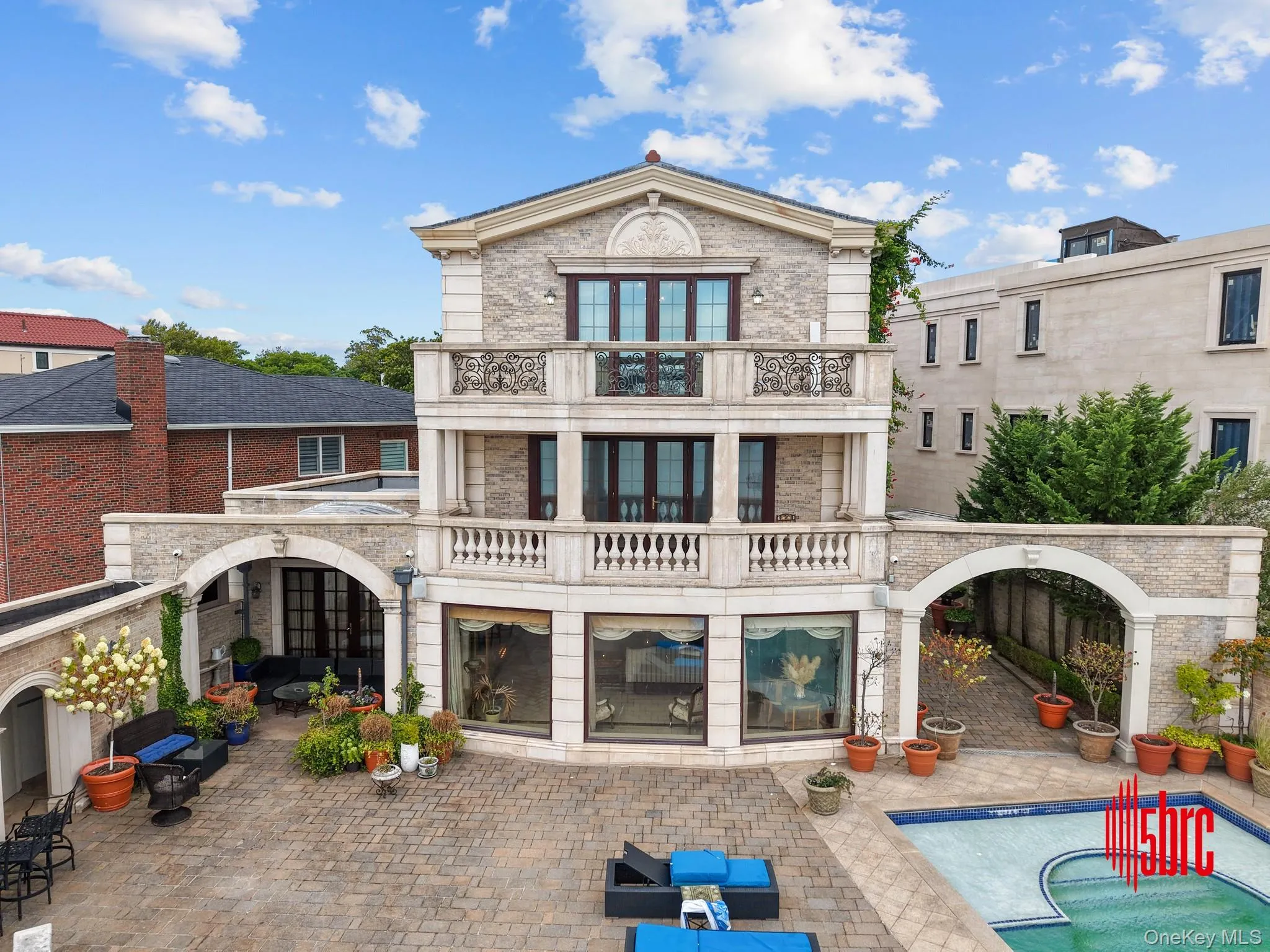 Rear view of property with a balcony, a patio area, stone siding, and an outdoor pool Rear view of property with a balcony, a patio area, stone siding, and an outdoor pool