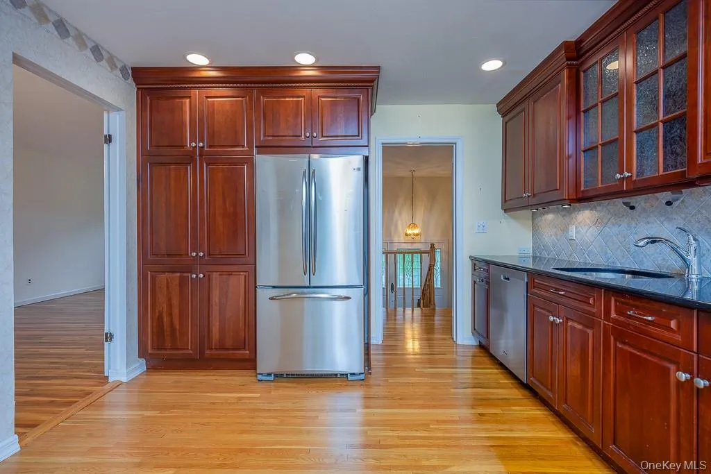 Kitchen featuring stainless steel appliances, a sink, light wood-type flooring, backsplash, and dark stone counters Kitchen featuring stainless steel appliances, a sink, light wood-type flooring, backsplash, and dark stone counters