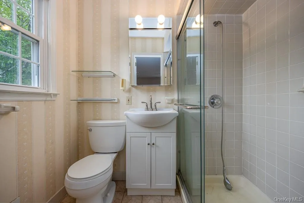Bathroom with a stall shower, vanity, toilet, and wallpapered walls Bathroom with a stall shower, vanity, toilet, and wallpapered walls