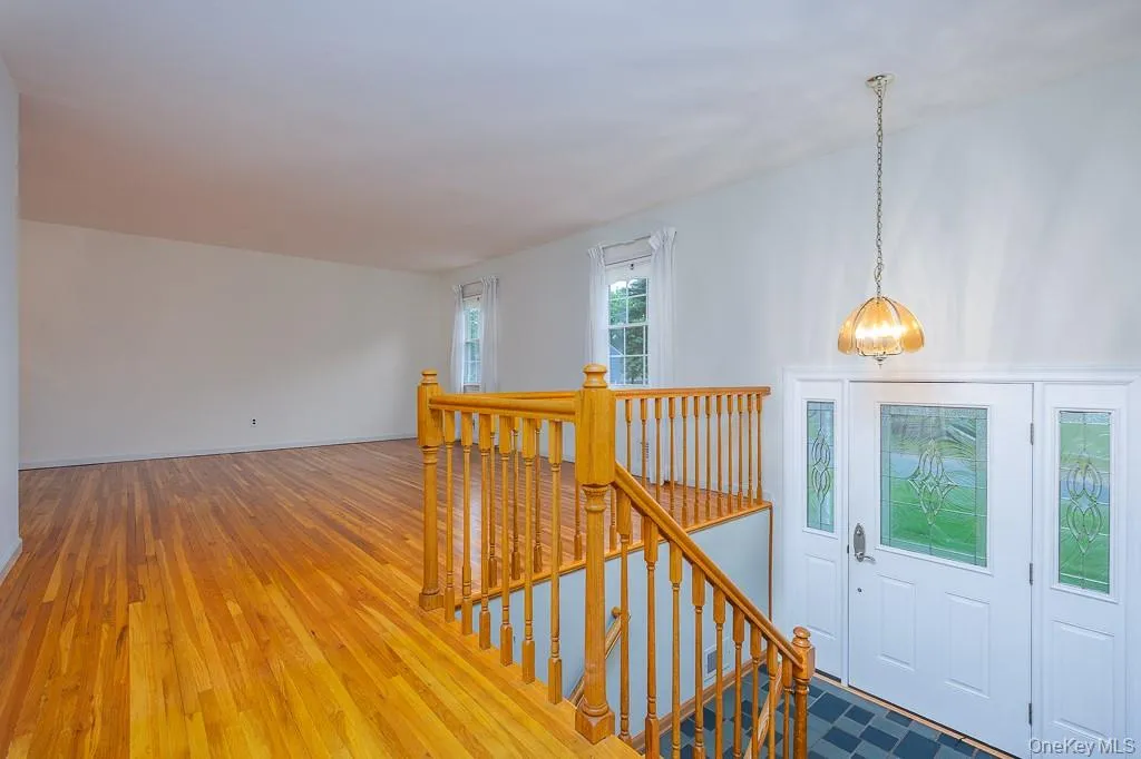 Hallway with an upstairs landing, a chandelier, light wood-style flooring, and baseboards Hallway with an upstairs landing, a chandelier, light wood-style flooring, and baseboards