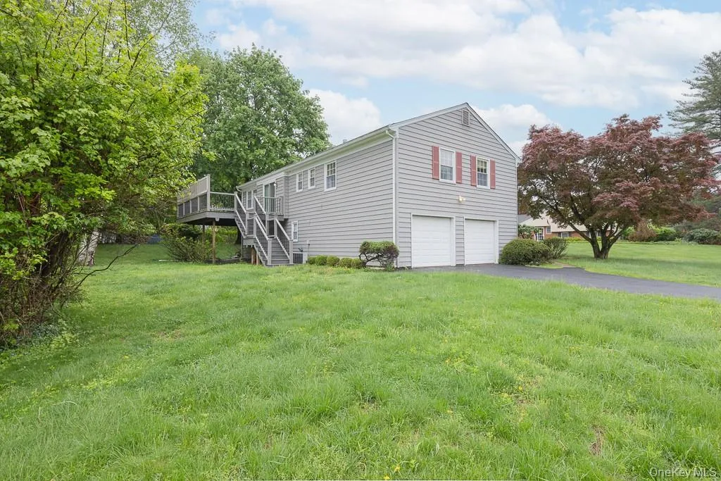 View of side of property featuring a garage, stairway, asphalt driveway, a wooden deck, and a yard View of side of property featuring a garage, stairway, asphalt driveway, a wooden deck, and a yard