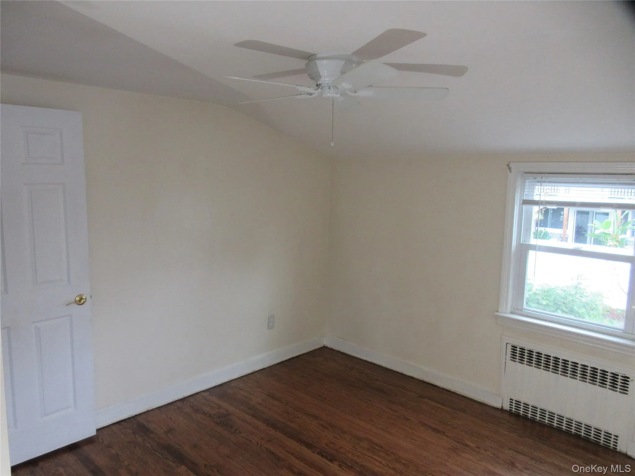 Empty room with dark wood-style flooring, radiator heating unit, lofted ceiling, and a ceiling fan Empty room with dark wood-style flooring, radiator heating unit, lofted ceiling, and a ceiling fan