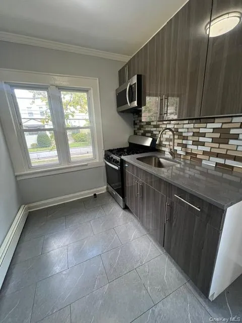 Kitchen featuring decorative backsplash, modern cabinets, appliances with stainless steel finishes, dark stone countertops, and a baseboard radiator Kitchen featuring decorative backsplash, modern cabinets, appliances with stainless steel finishes, dark stone countertops, and a baseboard radiator