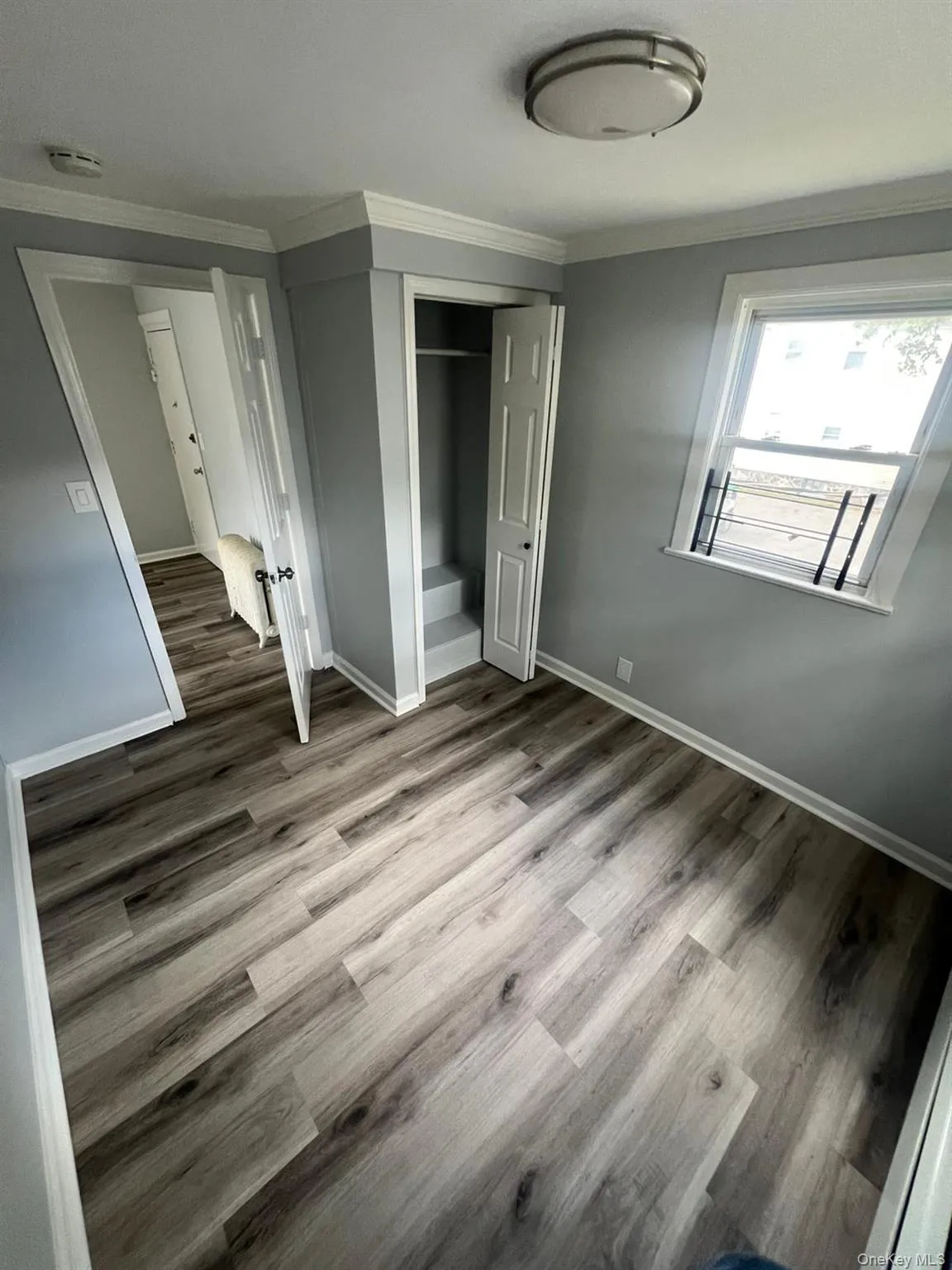 Unfurnished bedroom with ornamental molding, a closet, and light wood-style floors Unfurnished bedroom with ornamental molding, a closet, and light wood-style floors