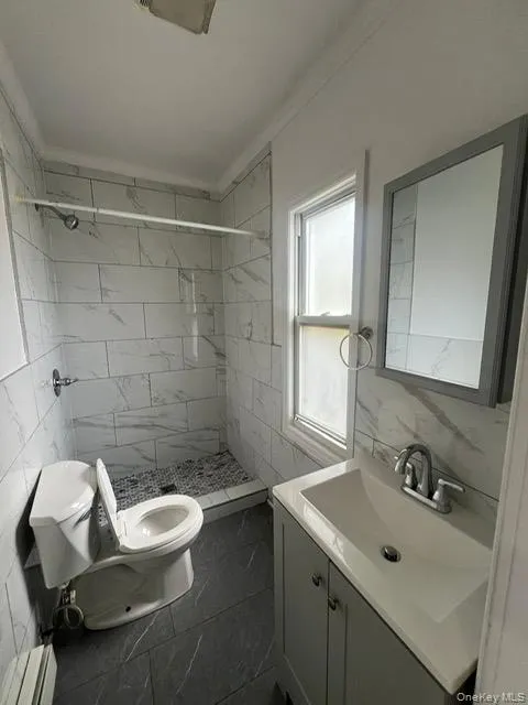 Bathroom with vanity, tile walls, a stall shower, a baseboard radiator, and crown molding Bathroom with vanity, tile walls, a stall shower, a baseboard radiator, and crown molding