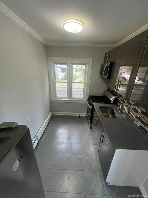 Kitchen with gas range, healthy amount of natural light, crown molding, baseboard heating, and stainless steel microwave Kitchen with gas range, healthy amount of natural light, crown molding, baseboard heating, and stainless steel microwave