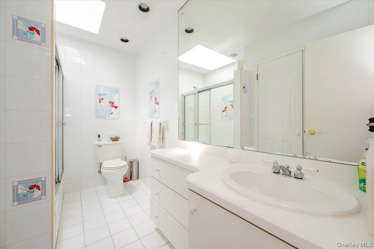 Full bath with a skylight, light tile patterned flooring, tile walls, and a shower with shower door Full bath with a skylight, light tile patterned flooring, tile walls, and a shower with shower door