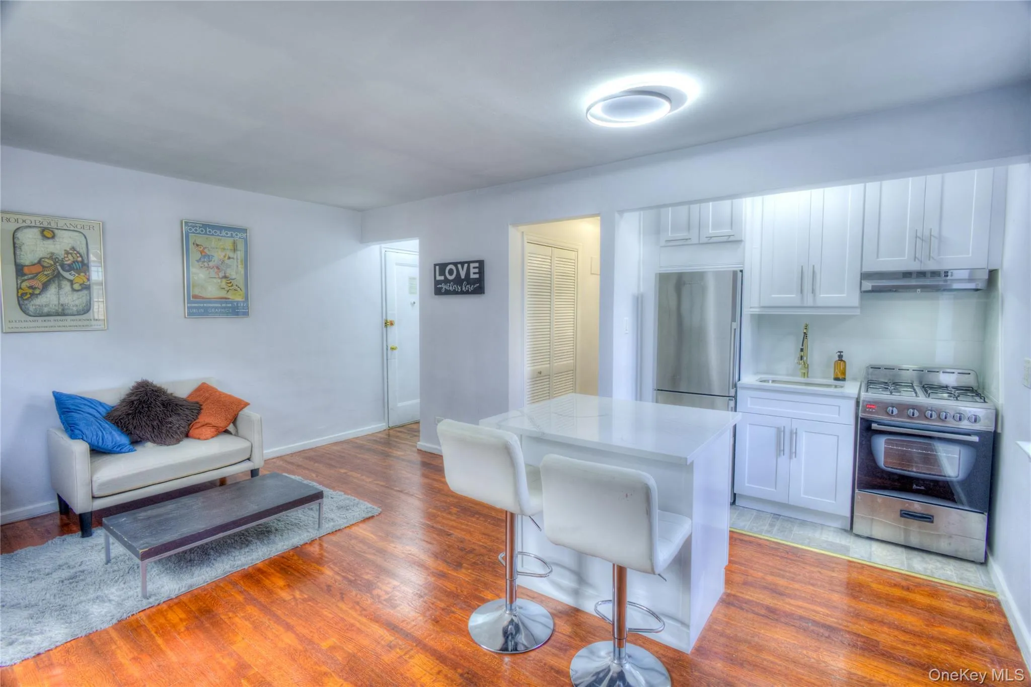Kitchen featuring appliances with stainless steel finishes, light wood-style floors, white cabinetry, and a kitchen bar Kitchen featuring appliances with stainless steel finishes, light wood-style floors, white cabinetry, and a kitchen bar