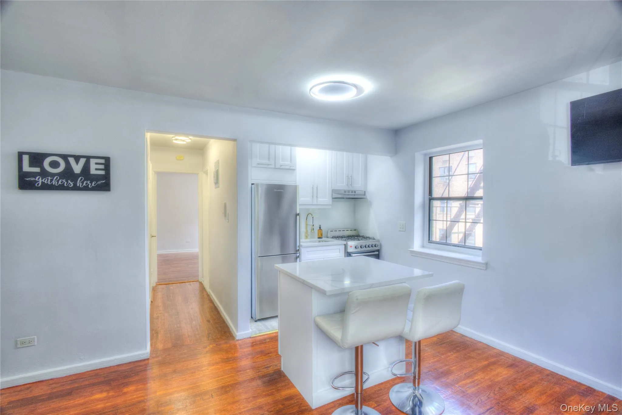 Kitchen featuring freestanding refrigerator, dark wood-style flooring, a breakfast bar area, white cabinets, and white gas stove Kitchen featuring freestanding refrigerator, dark wood-style flooring, a breakfast bar area, white cabinets, and white gas stove