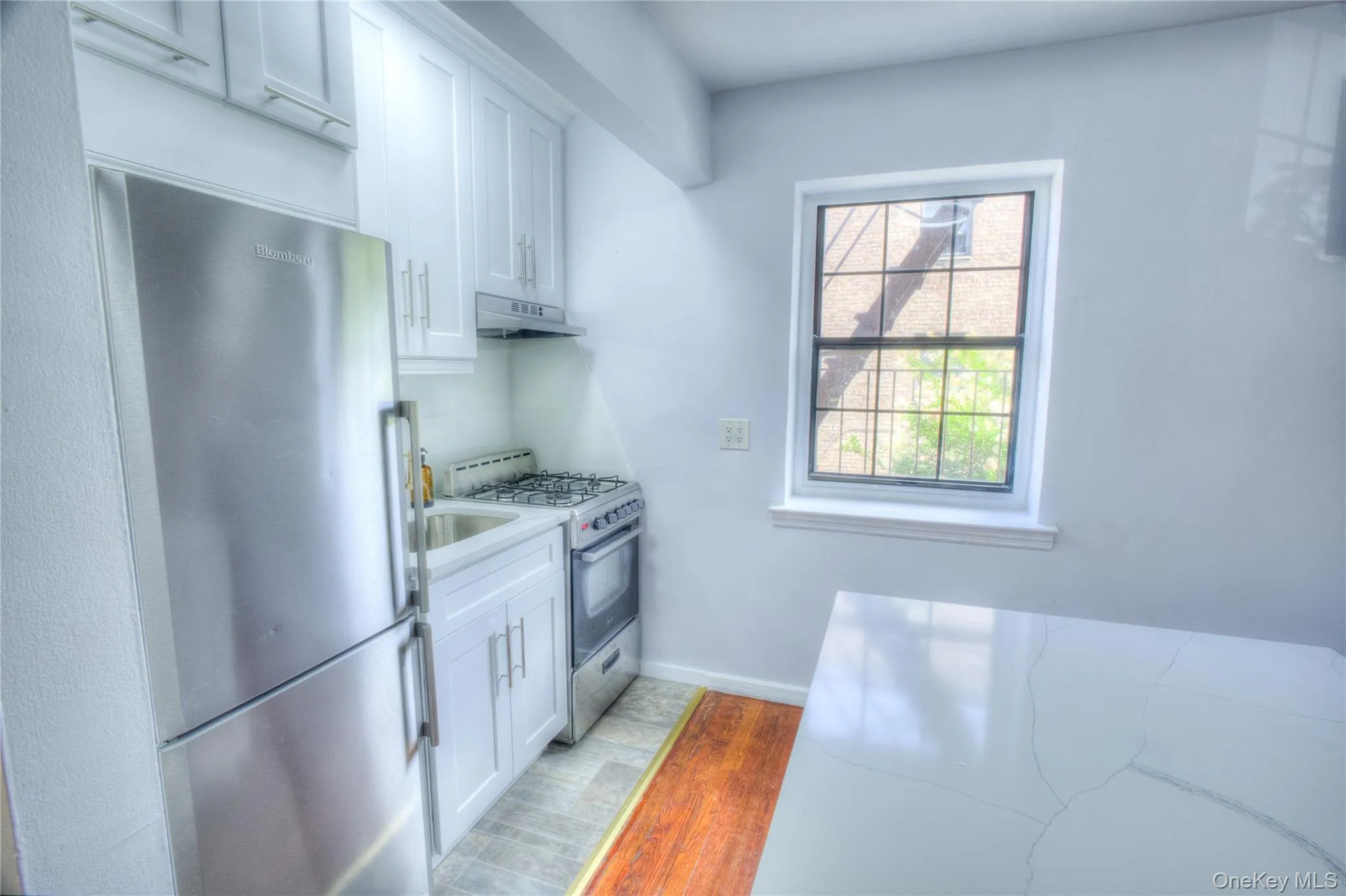 Kitchen featuring stainless steel appliances, white cabinetry, light wood-style flooring, and under cabinet range hood Kitchen featuring stainless steel appliances, white cabinetry, light wood-style flooring, and under cabinet range hood