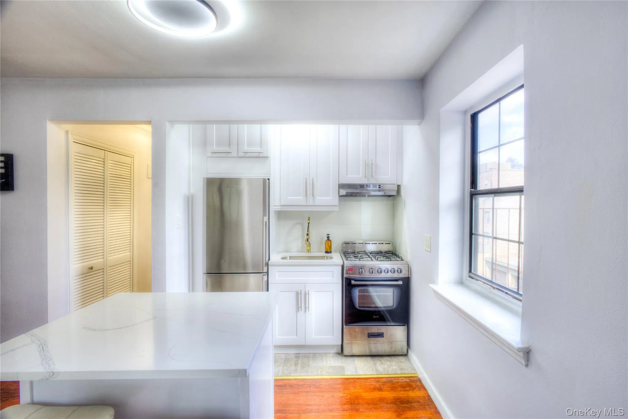 Kitchen featuring appliances with stainless steel finishes, white cabinets, light wood-style floors, and under cabinet range hood Kitchen featuring appliances with stainless steel finishes, white cabinets, light wood-style floors, and under cabinet range hood
