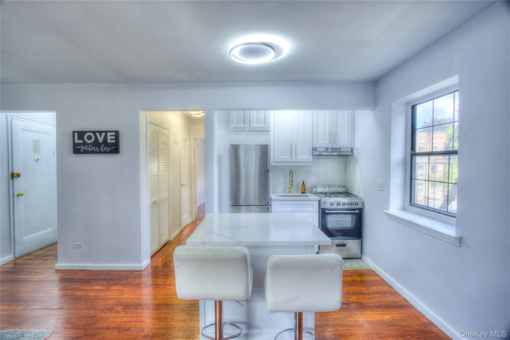 Kitchen featuring white cabinets, stainless steel appliances, a breakfast bar area, dark wood-style flooring, and light stone countertops Kitchen featuring white cabinets, stainless steel appliances, a breakfast bar area, dark wood-style flooring, and light stone countertops