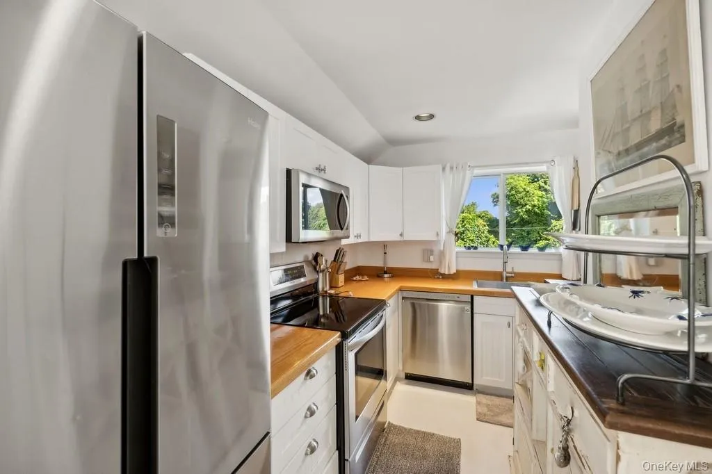Kitchen featuring appliances with stainless steel finishes, white cabinetry, lofted ceiling, recessed lighting, and wooden counters Kitchen featuring appliances with stainless steel finishes, white cabinetry, lofted ceiling, recessed lighting, and wooden counters
