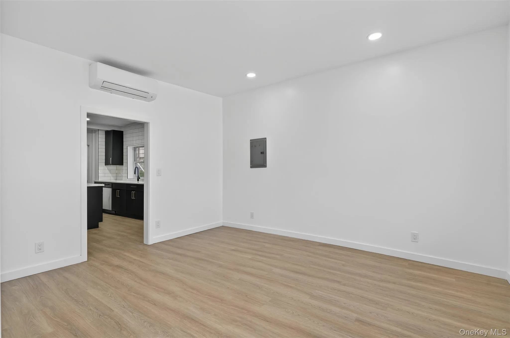 Empty room with light wood-style floors, a wall mounted air conditioner, recessed lighting, and electric panel Empty room with light wood-style floors, a wall mounted air conditioner, recessed lighting, and electric panel