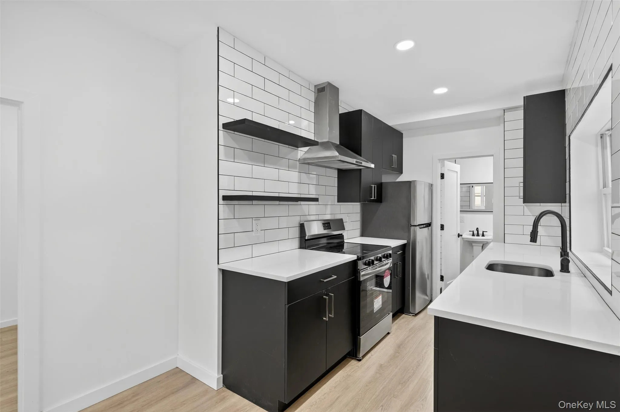 Kitchen with dark cabinets, electric range, light wood-type flooring, decorative backsplash, and recessed lighting Kitchen with dark cabinets, electric range, light wood-type flooring, decorative backsplash, and recessed lighting