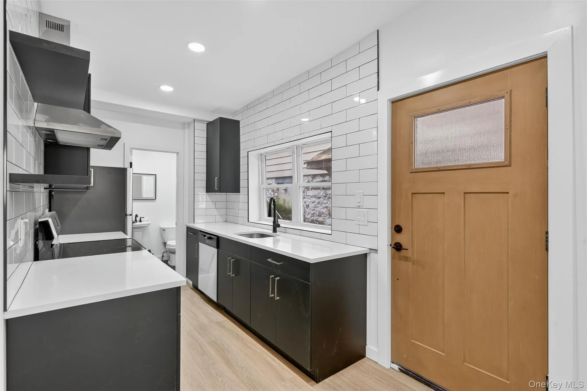 Kitchen with dark cabinetry, decorative backsplash, light stone counters, light wood finished floors, and extractor fan Kitchen with dark cabinetry, decorative backsplash, light stone counters, light wood finished floors, and extractor fan