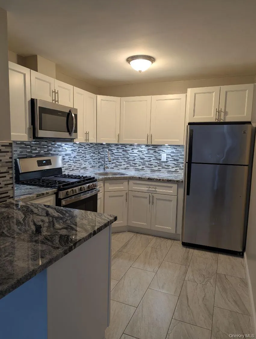 Kitchen featuring dark stone counters, stainless steel appliances, decorative backsplash, and white cabinetry Kitchen featuring dark stone counters, stainless steel appliances, decorative backsplash, and white cabinetry