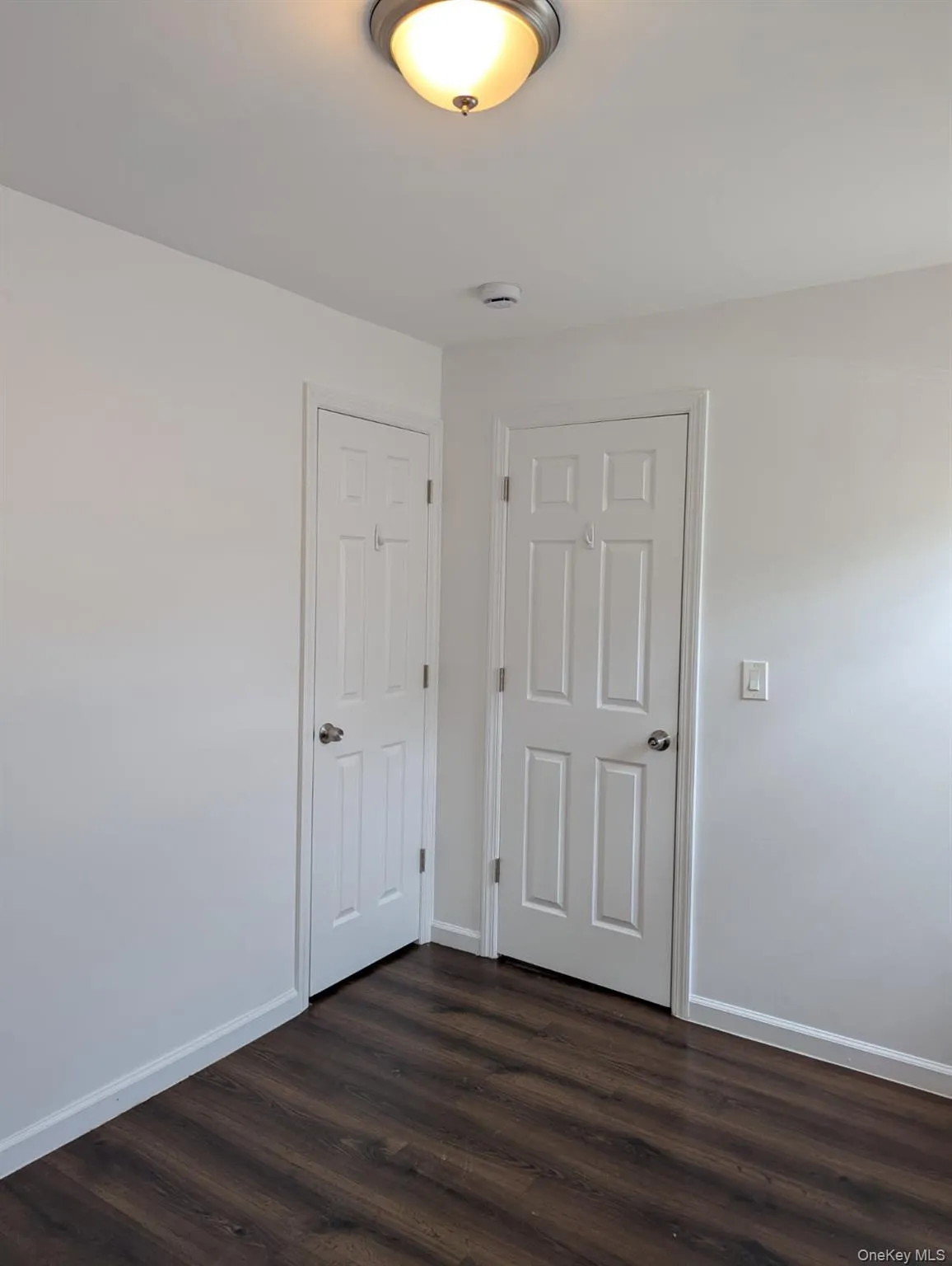 Unfurnished bedroom featuring dark wood-type flooring and baseboards Unfurnished bedroom featuring dark wood-type flooring and baseboards