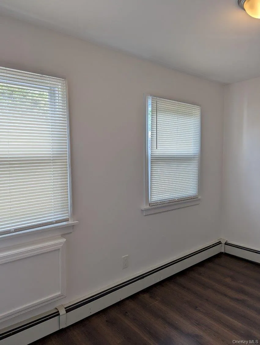 Spare room featuring baseboard heating, healthy amount of natural light, and dark wood-type flooring Spare room featuring baseboard heating, healthy amount of natural light, and dark wood-type flooring