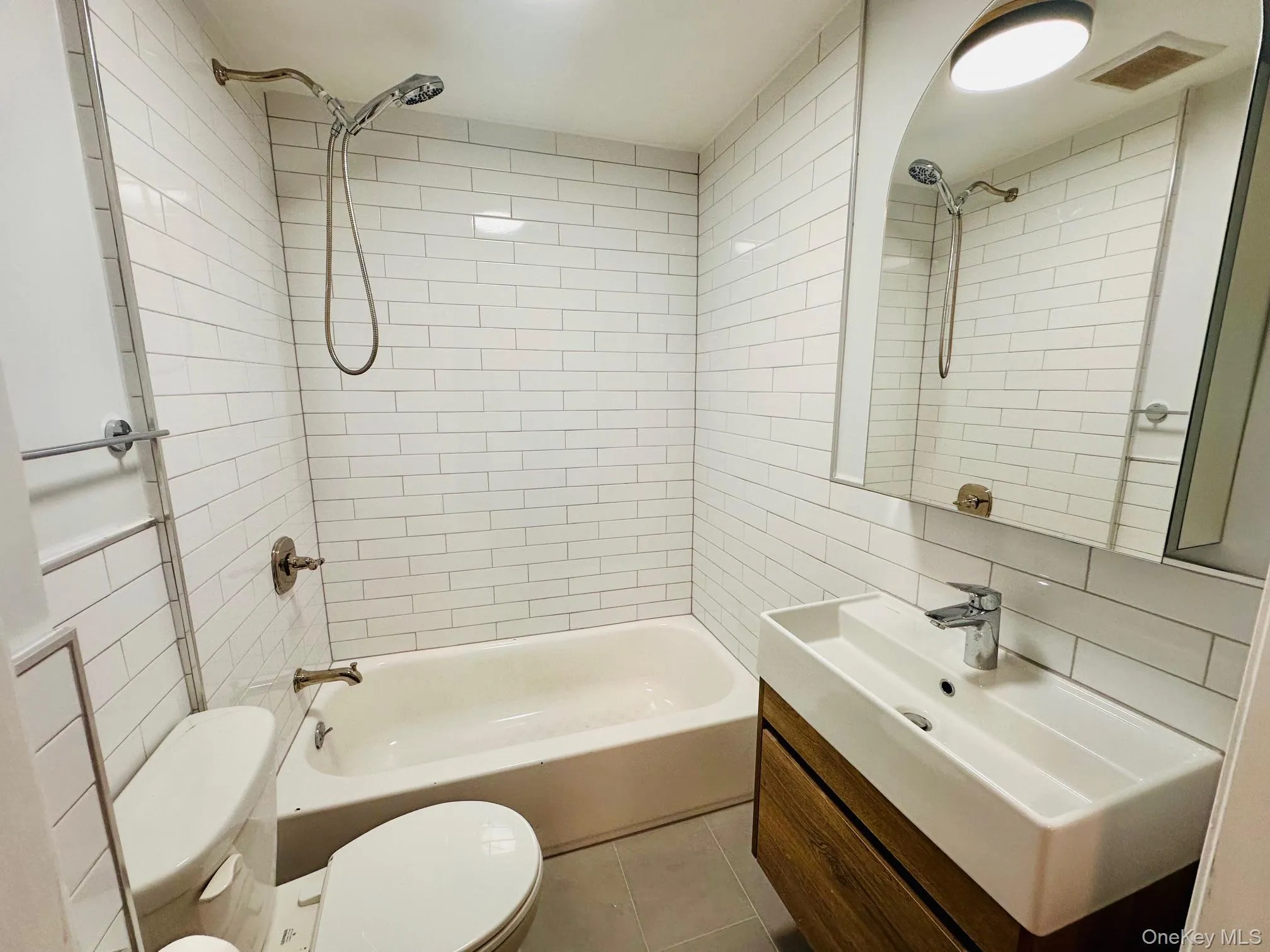 Bathroom featuring tile walls, bathtub / shower combination, vanity, and light tile patterned floors Bathroom featuring tile walls, bathtub / shower combination, vanity, and light tile patterned floors