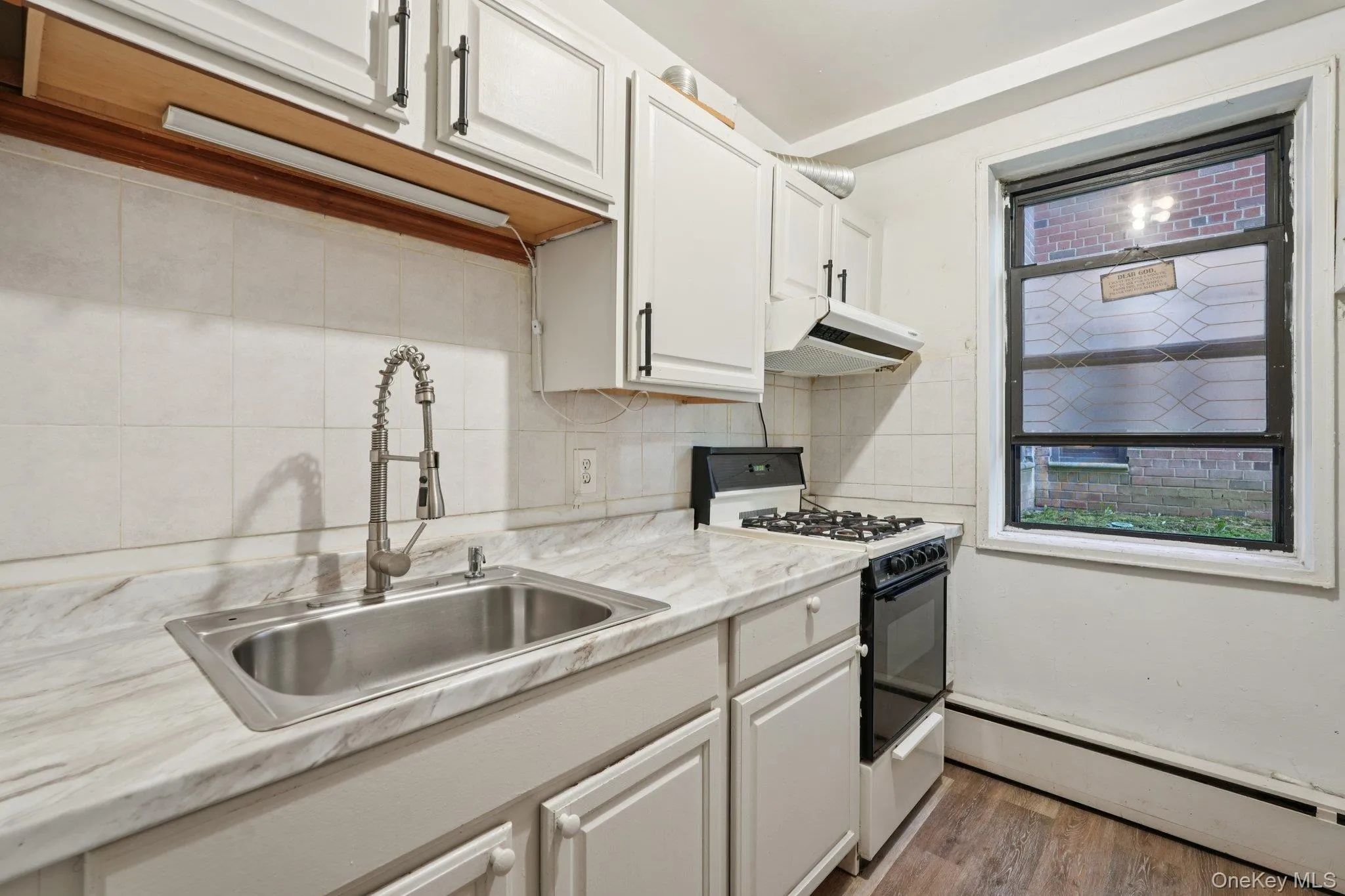 Kitchen with light countertops, baseboard heating, gas range, backsplash, and light wood-type flooring Kitchen with light countertops, baseboard heating, gas range, backsplash, and light wood-type flooring