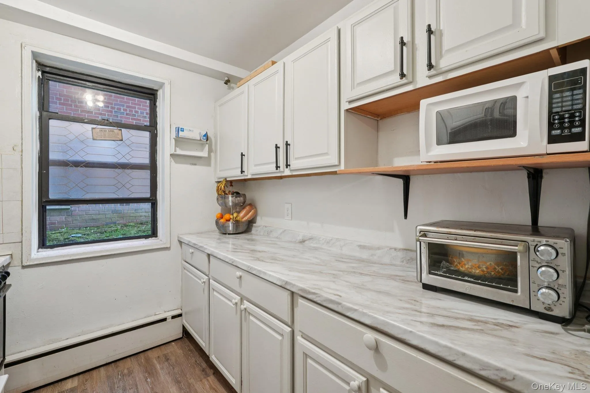 Kitchen featuring a baseboard radiator, white cabinets, light wood-style floors, white microwave, and open shelves Kitchen featuring a baseboard radiator, white cabinets, light wood-style floors, white microwave, and open shelves