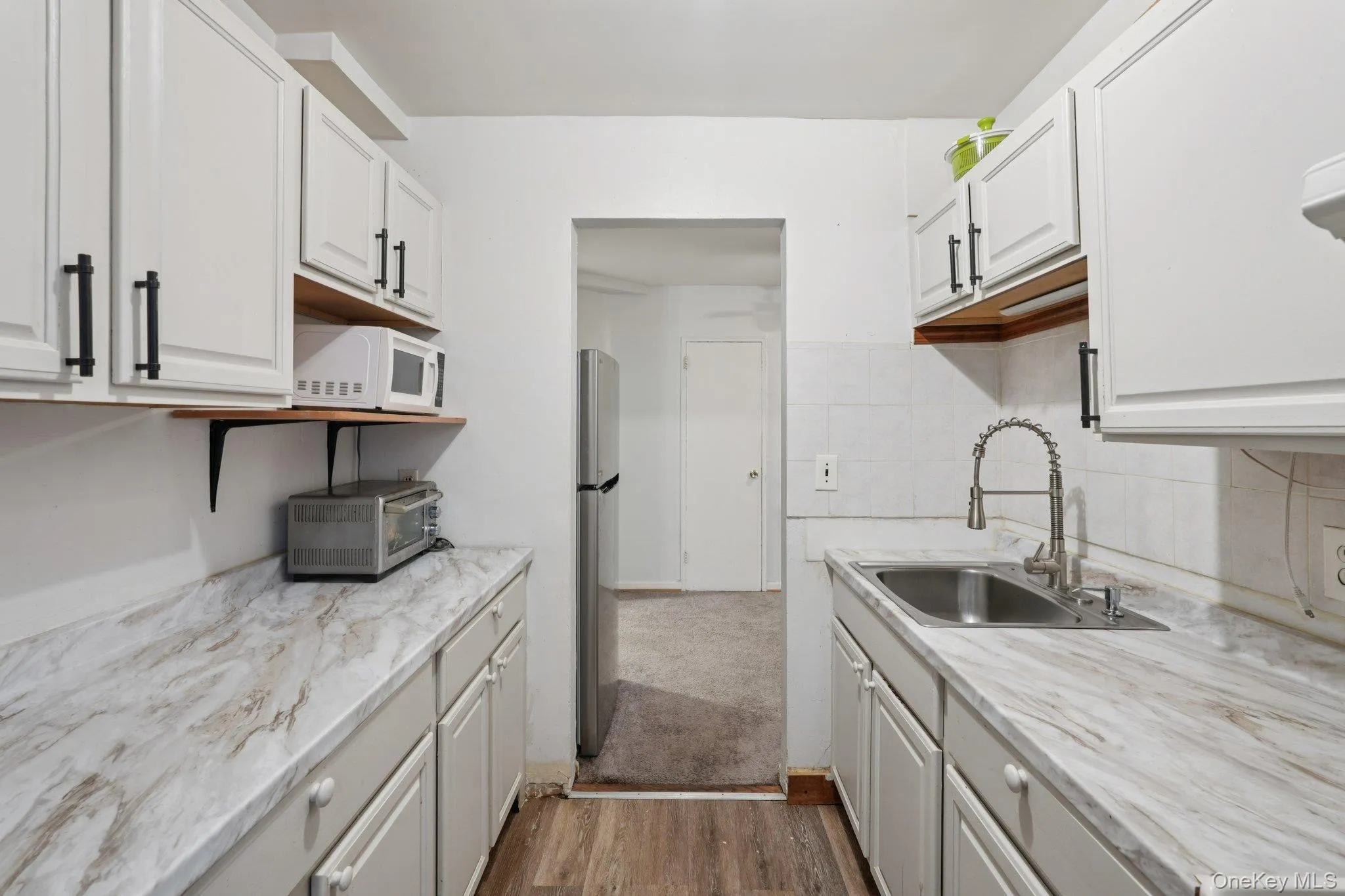 Kitchen with dark wood-style flooring, white cabinetry, white microwave, and freestanding refrigerator Kitchen with dark wood-style flooring, white cabinetry, white microwave, and freestanding refrigerator