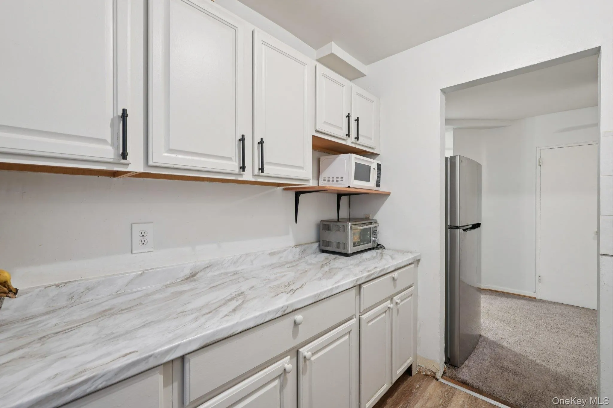 Kitchen featuring white cabinets, white microwave, freestanding refrigerator, dark wood finished floors, and open shelves Kitchen featuring white cabinets, white microwave, freestanding refrigerator, dark wood finished floors, and open shelves