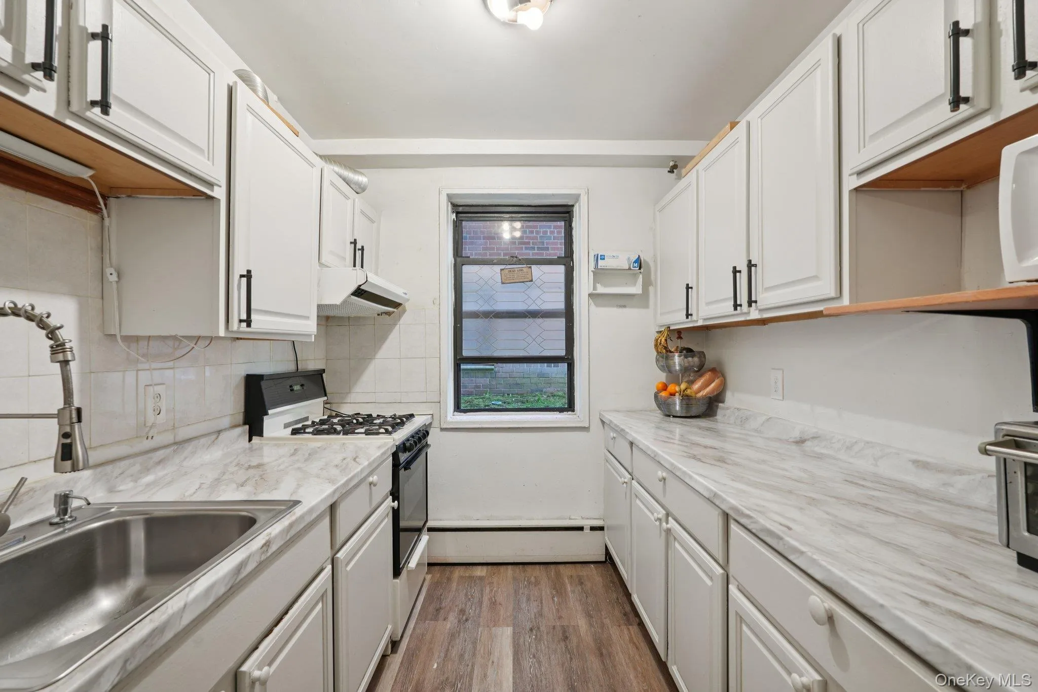Kitchen with gas range oven, light wood finished floors, and white cabinetry Kitchen with gas range oven, light wood finished floors, and white cabinetry
