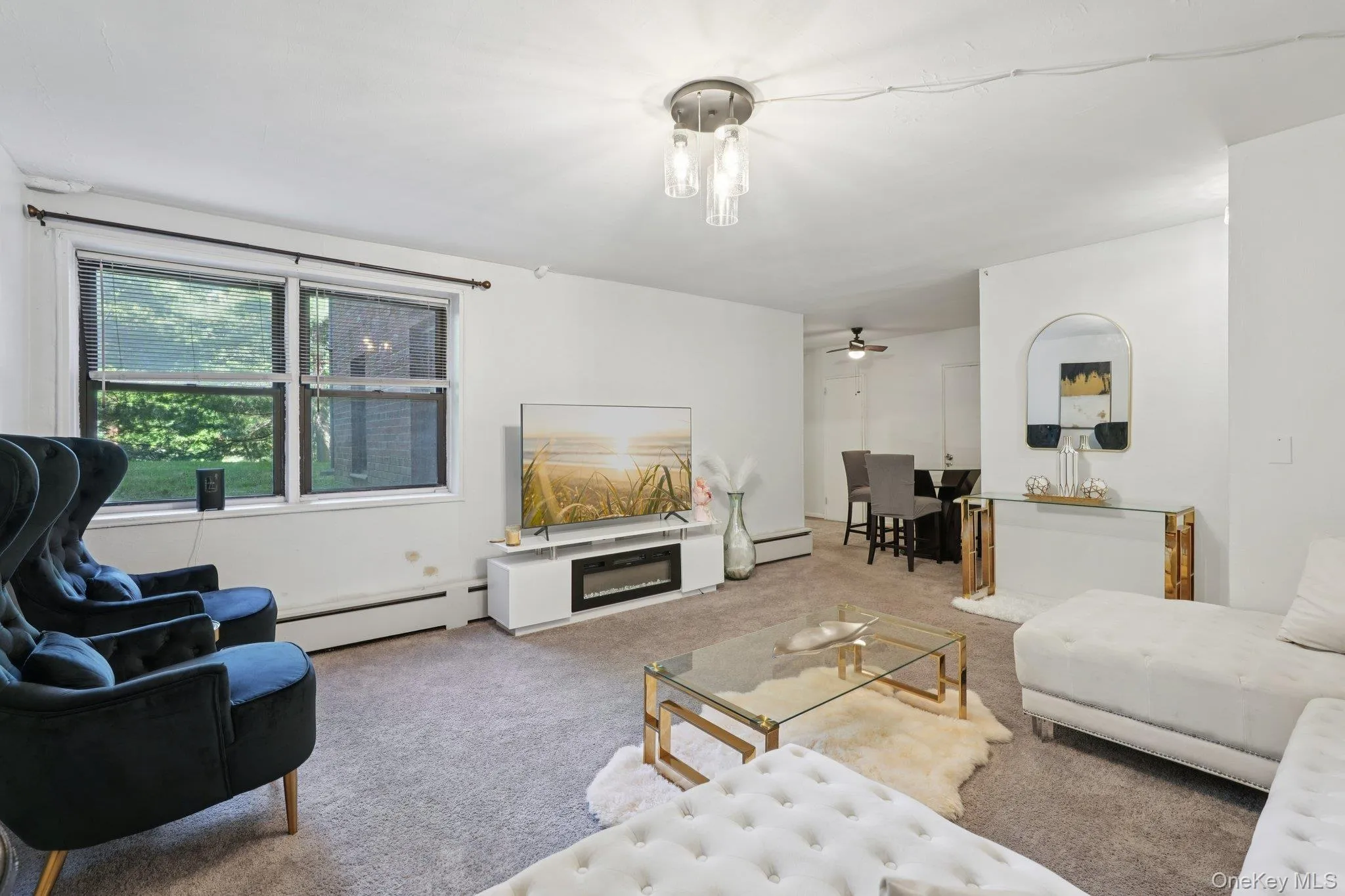 Carpeted living room with a baseboard heating unit, ceiling fan, and a glass covered fireplace Carpeted living room with a baseboard heating unit, ceiling fan, and a glass covered fireplace