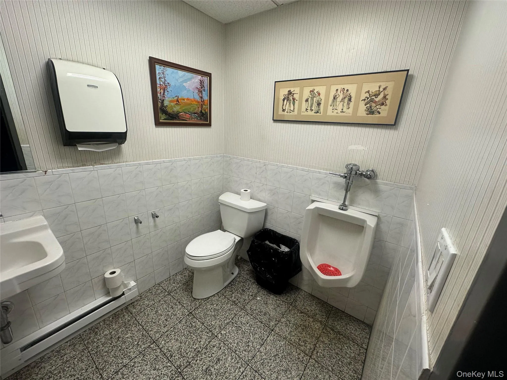 Bathroom featuring baseboard heating, tile walls, wainscoting, and wallpapered walls Bathroom featuring baseboard heating, tile walls, wainscoting, and wallpapered walls