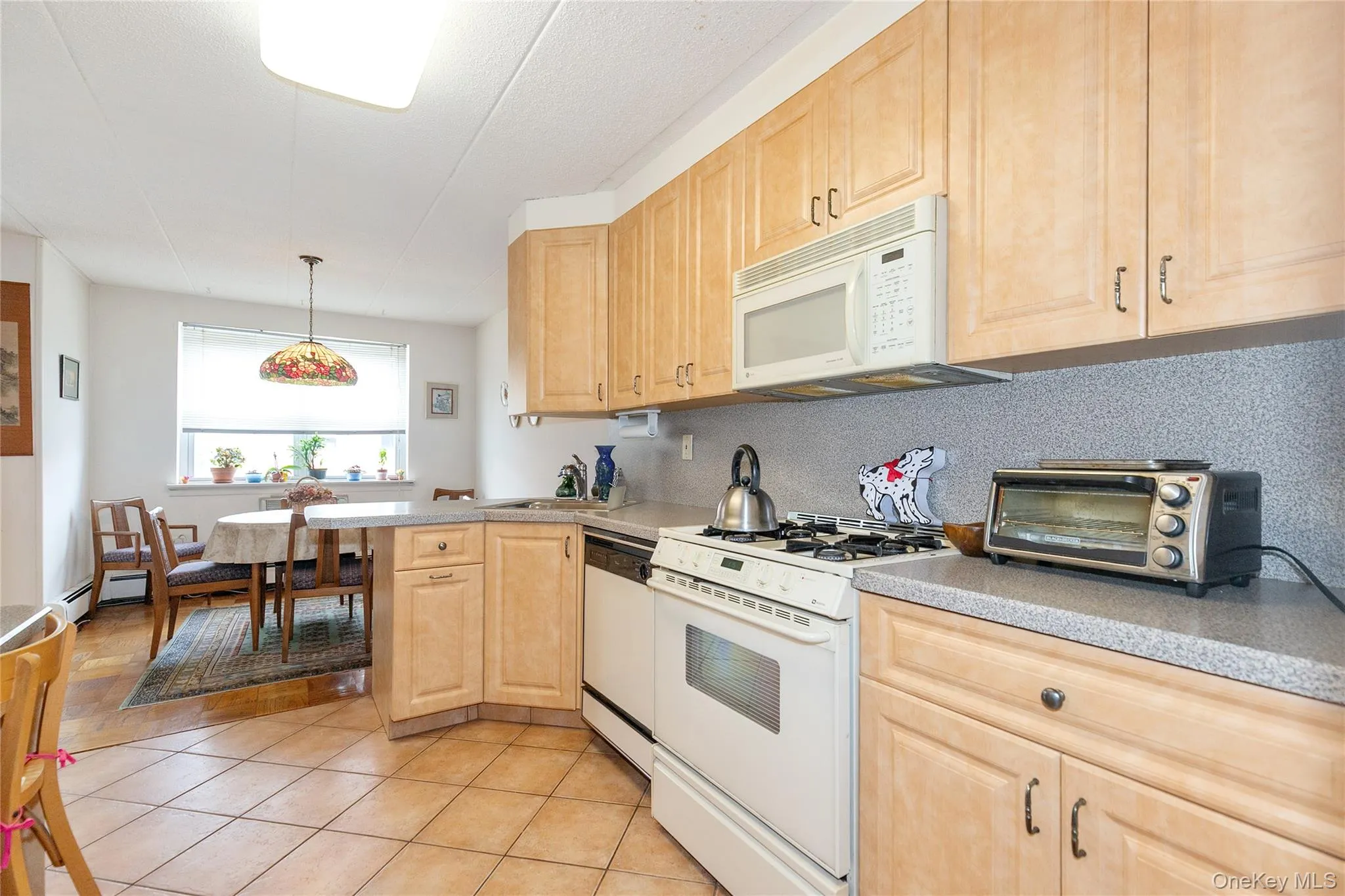 Kitchen with white appliances, light brown cabinetry, light tile patterned floors, tasteful backsplash, and light countertops Kitchen with white appliances, light brown cabinetry, light tile patterned floors, tasteful backsplash, and light countertops