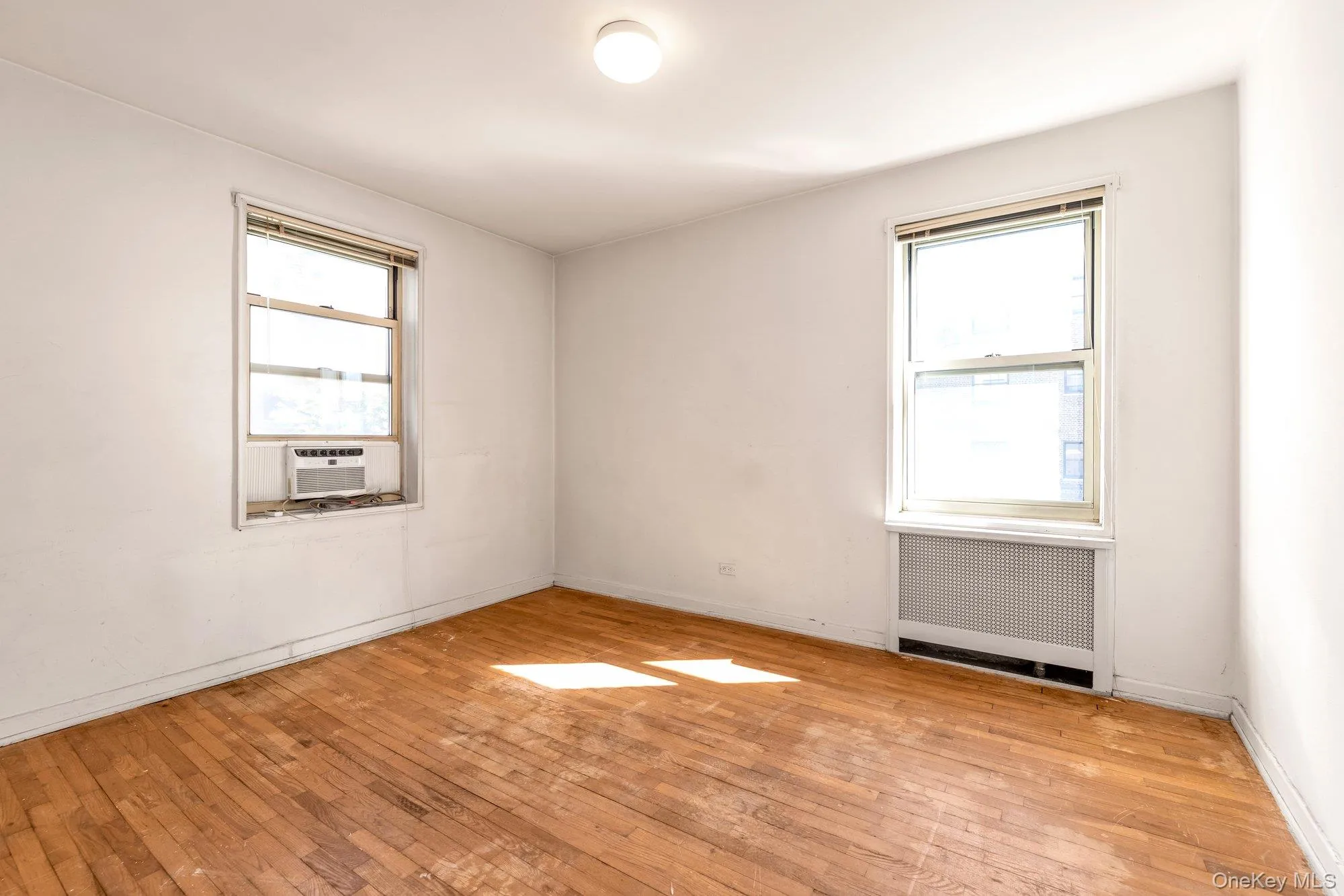 Empty room with radiator heating unit, light wood finished floors, and plenty of natural light Empty room with radiator heating unit, light wood finished floors, and plenty of natural light