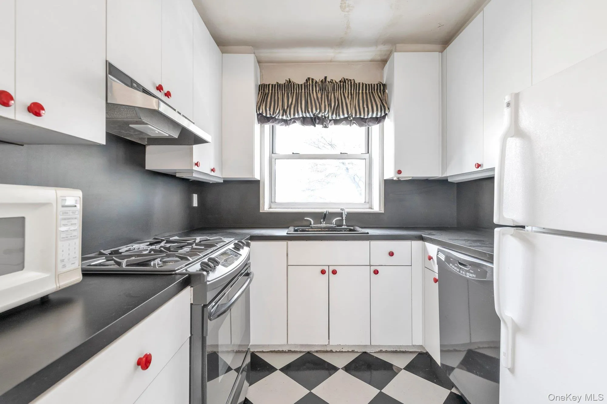 Kitchen featuring white appliances, dark countertops, light flooring, and under cabinet range hood Kitchen featuring white appliances, dark countertops, light flooring, and under cabinet range hood