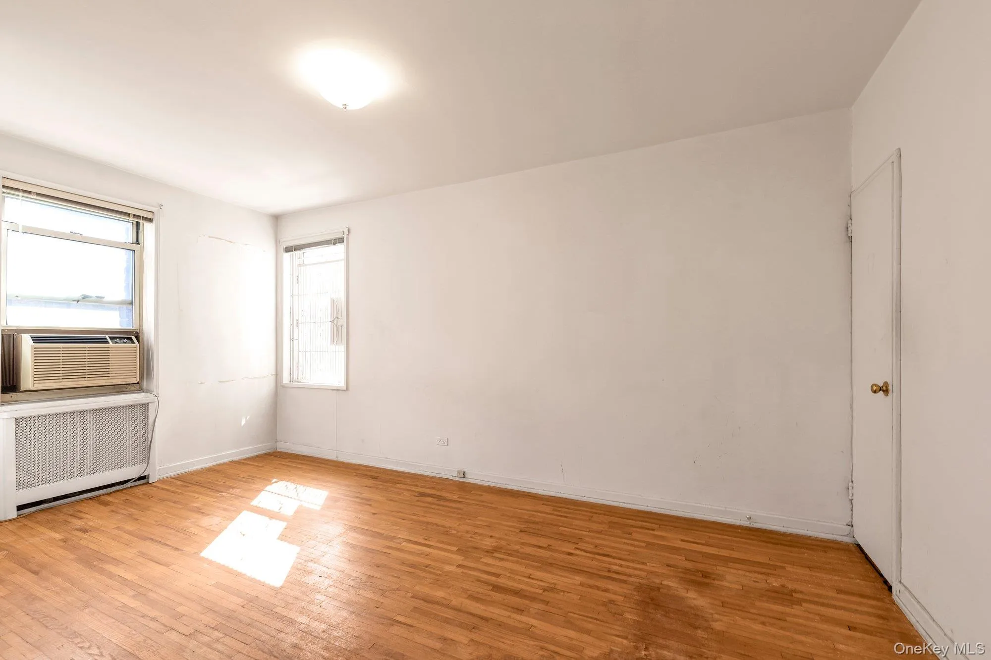 Unfurnished room with radiator heating unit, light wood-style flooring, and cooling unit Unfurnished room with radiator heating unit, light wood-style flooring, and cooling unit