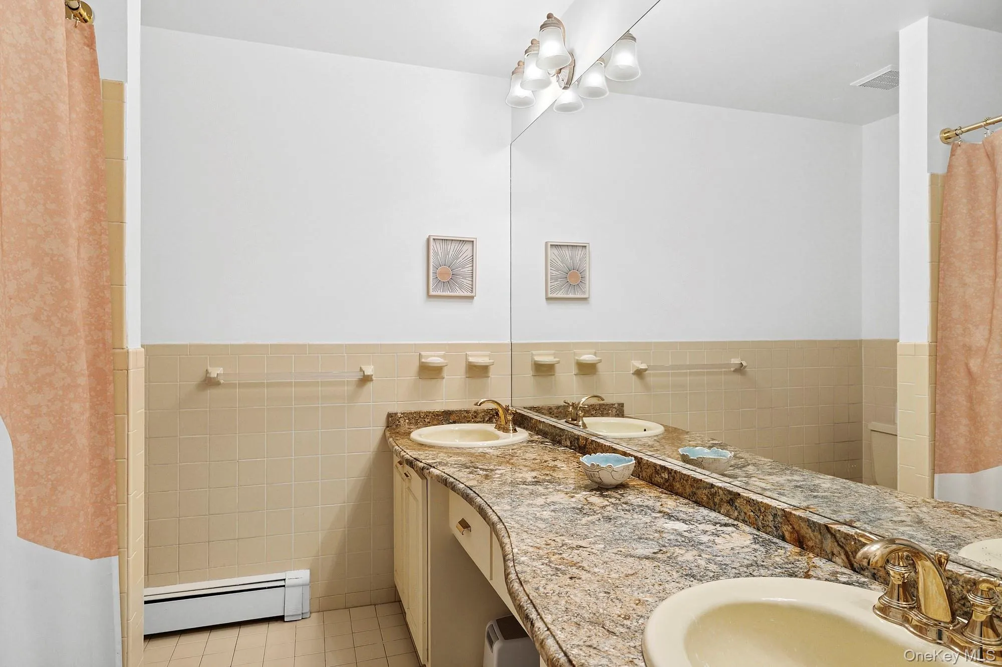 Full bath with tile walls, baseboard heating, light tile patterned flooring, double vanity, and wainscoting Full bath with tile walls, baseboard heating, light tile patterned flooring, double vanity, and wainscoting
