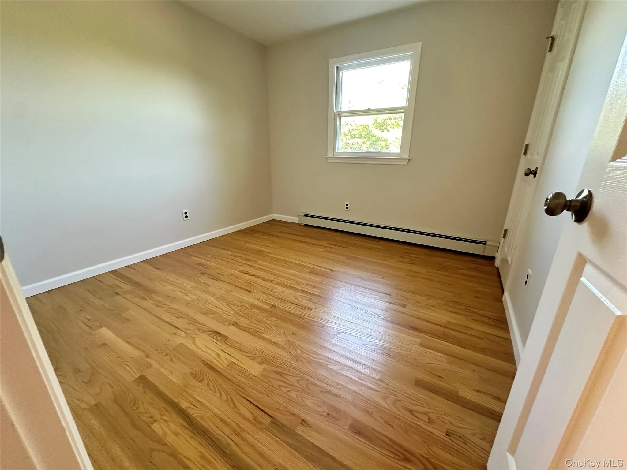 Unfurnished bedroom with light wood-type flooring and baseboard heating Unfurnished bedroom with light wood-type flooring and baseboard heating