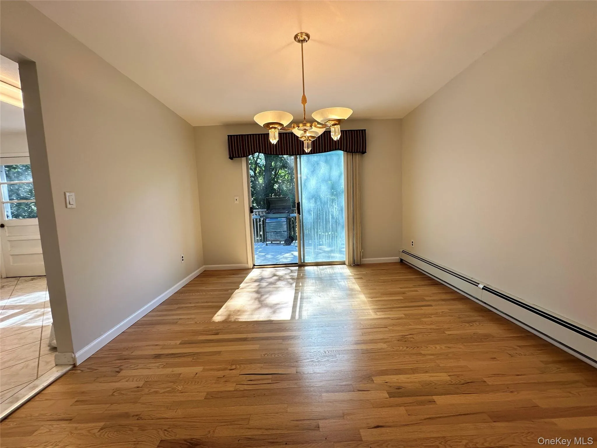Unfurnished dining area featuring a chandelier, light wood-style flooring, and a baseboard heating unit Unfurnished dining area featuring a chandelier, light wood-style flooring, and a baseboard heating unit