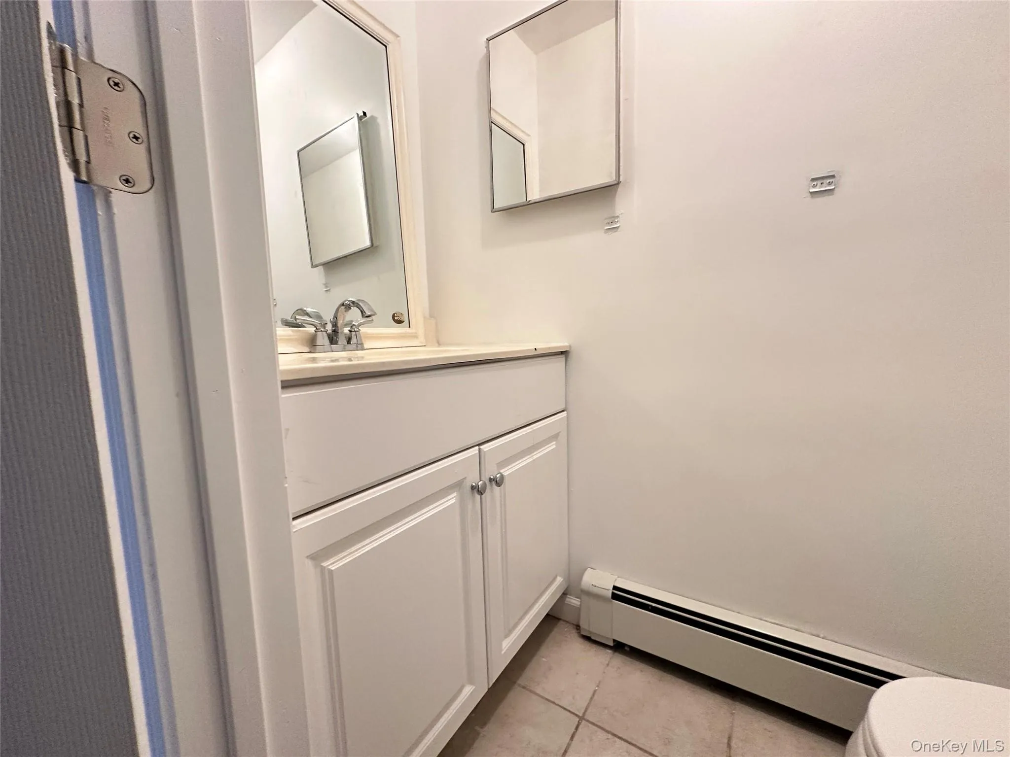Half bathroom featuring a baseboard heating unit, vanity, and light tile patterned floors Half bathroom featuring a baseboard heating unit, vanity, and light tile patterned floors