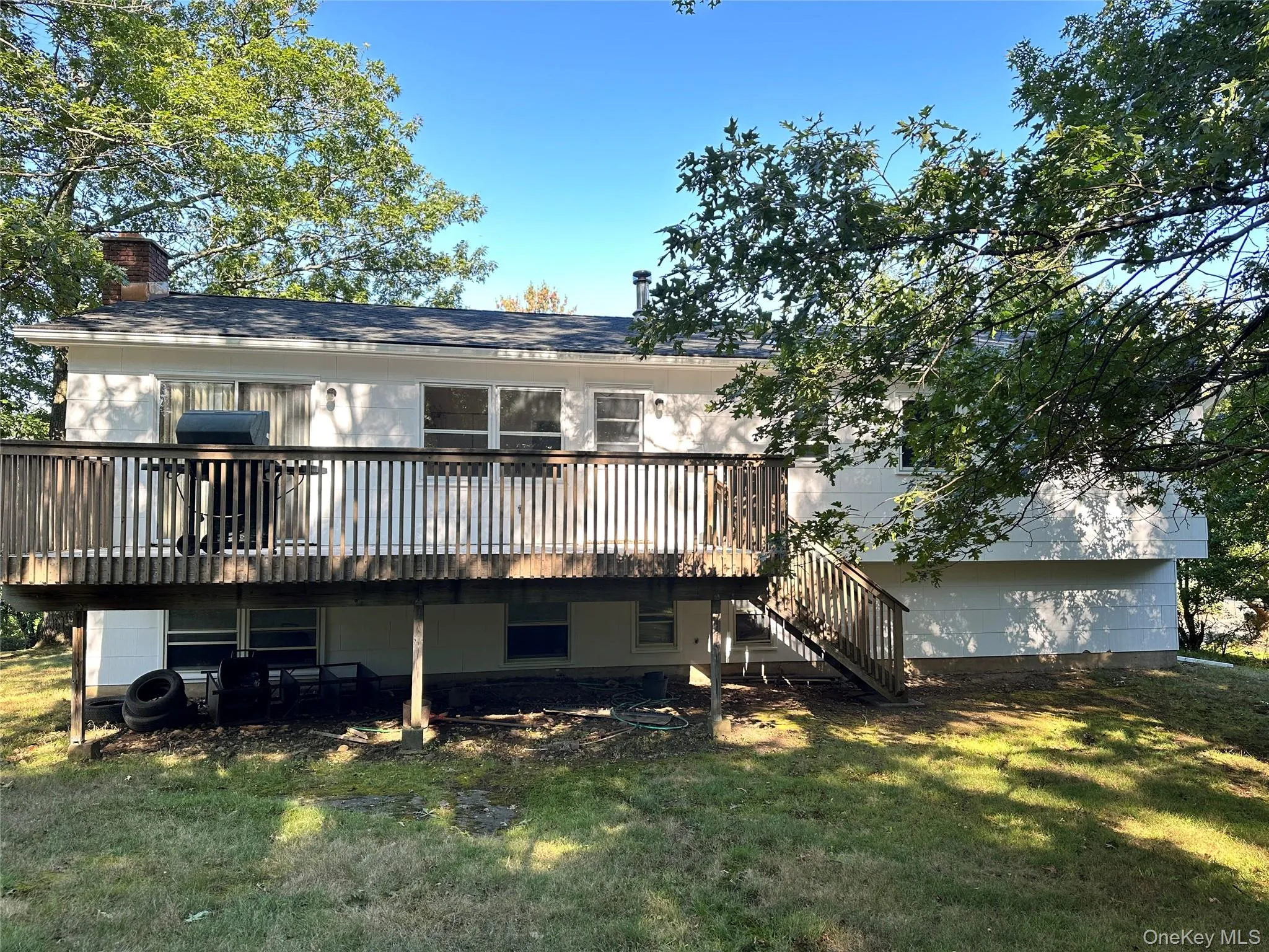 Rear view of house featuring a wooden deck, a chimney, a lawn, and stairway Rear view of house featuring a wooden deck, a chimney, a lawn, and stairway