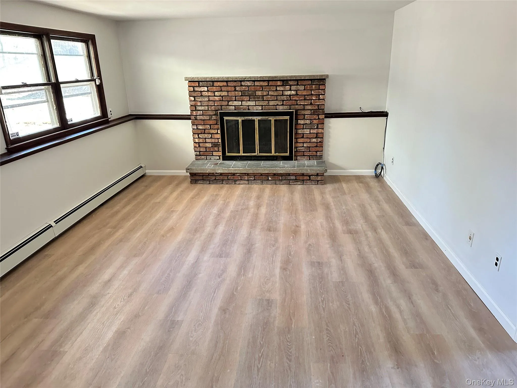 Unfurnished living room with a fireplace, light wood-style flooring, and baseboard heating Unfurnished living room with a fireplace, light wood-style flooring, and baseboard heating