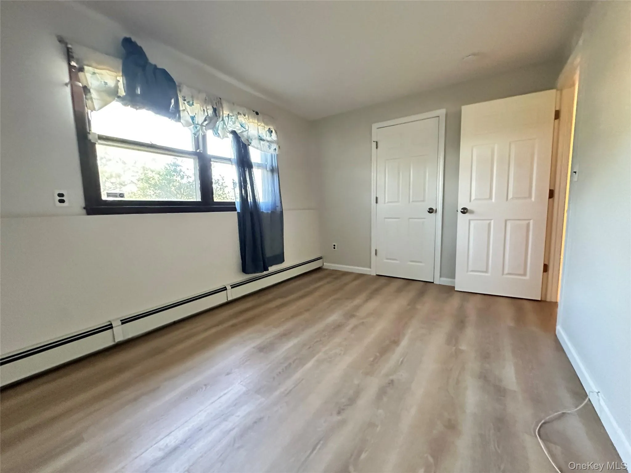 Unfurnished bedroom featuring a baseboard heating unit and light wood-style floors Unfurnished bedroom featuring a baseboard heating unit and light wood-style floors