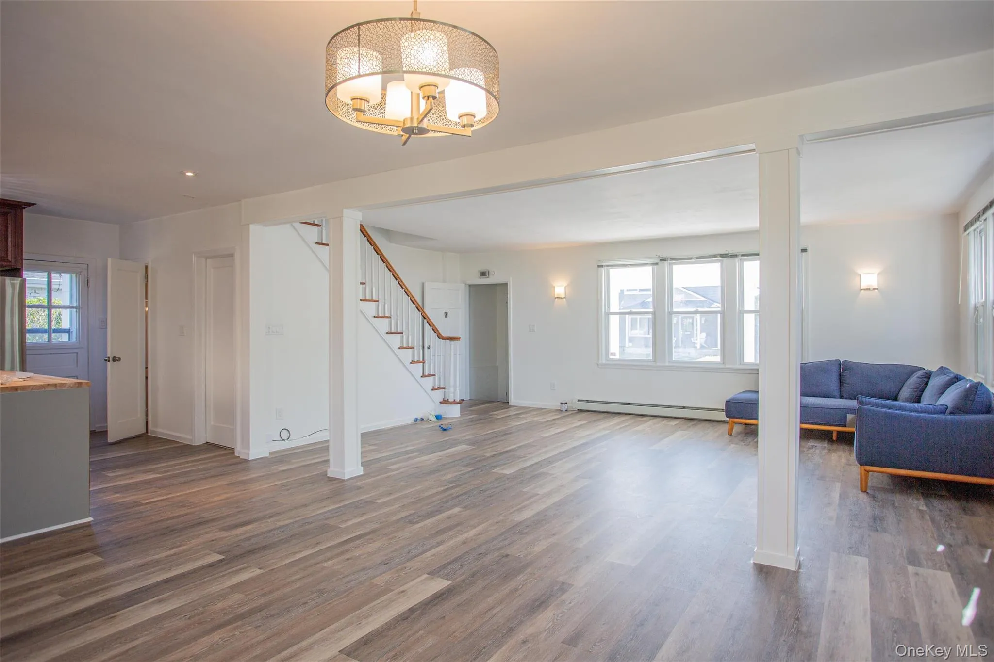 Living room featuring dark wood-style floors, stairway, and a baseboard heating unit Living room featuring dark wood-style floors, stairway, and a baseboard heating unit