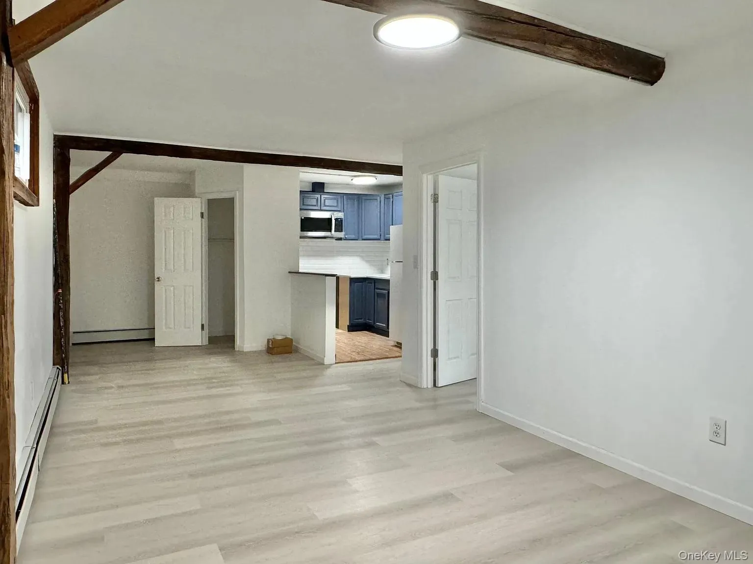 Unfurnished living room featuring beamed ceiling, a baseboard heating unit, and light wood-type flooring Unfurnished living room featuring beamed ceiling, a baseboard heating unit, and light wood-type flooring