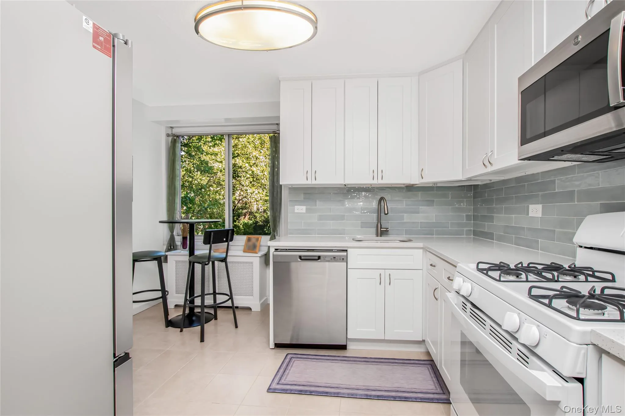 Kitchen featuring appliances with stainless steel finishes, backsplash, white cabinetry, light tile patterned floors, and light stone counters Kitchen featuring appliances with stainless steel finishes, backsplash, white cabinetry, light tile patterned floors, and light stone counters