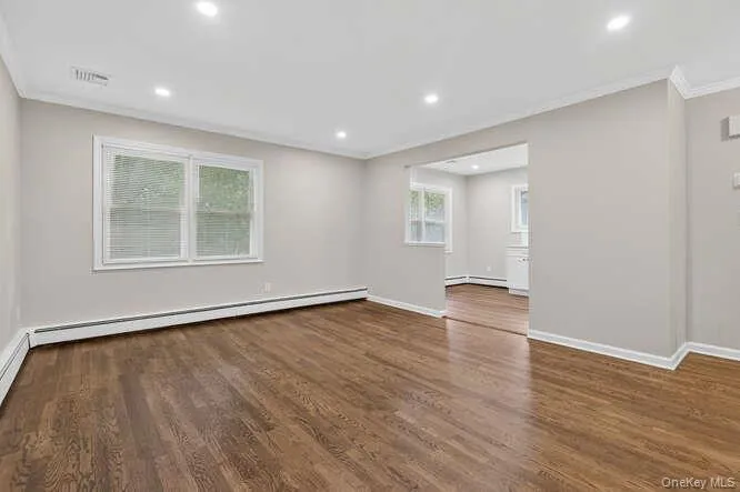 Unfurnished living room with ornamental molding, dark wood-type flooring, recessed lighting, and a baseboard radiator Unfurnished living room with ornamental molding, dark wood-type flooring, recessed lighting, and a baseboard radiator