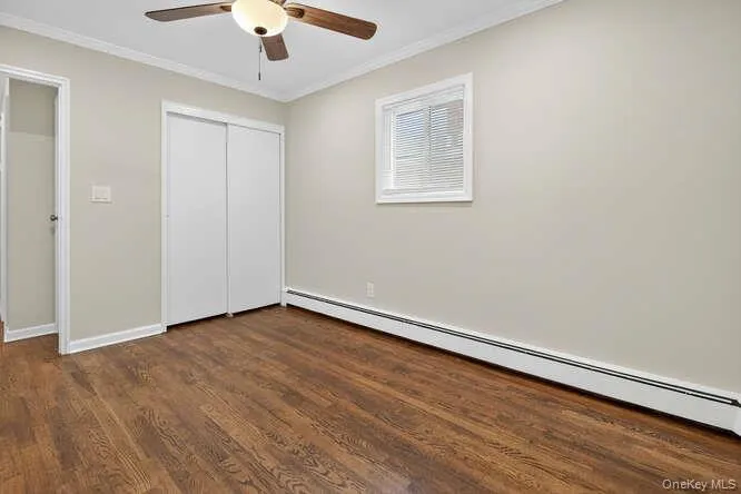 Unfurnished bedroom with a baseboard heating unit, crown molding, dark wood-style floors, ceiling fan, and a closet Unfurnished bedroom with a baseboard heating unit, crown molding, dark wood-style floors, ceiling fan, and a closet