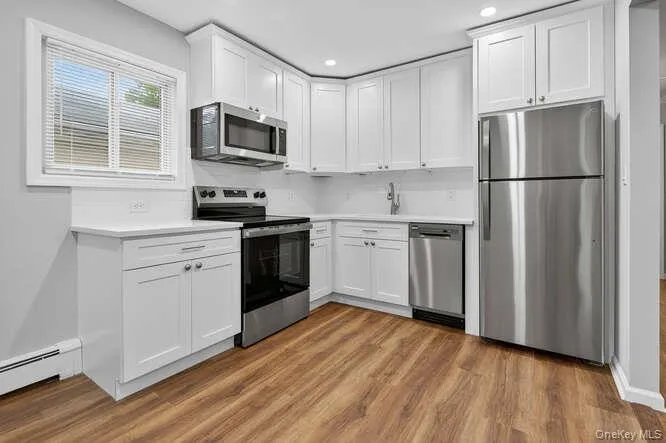 Kitchen featuring appliances with stainless steel finishes, light countertops, white cabinets, light wood-type flooring, and recessed lighting Kitchen featuring appliances with stainless steel finishes, light countertops, white cabinets, light wood-type flooring, and recessed lighting