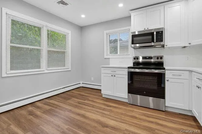 Kitchen featuring appliances with stainless steel finishes, white cabinets, light countertops, recessed lighting, and dark wood finished floors Kitchen featuring appliances with stainless steel finishes, white cabinets, light countertops, recessed lighting, and dark wood finished floors